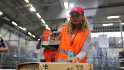 Symbolbild: Ina Fassbender/dpa
Eine Amazon-Mitarbeitern scannt ein Paket ein.