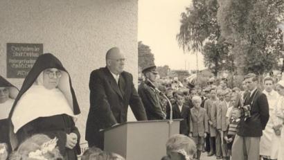 Bild: u
Als der von AKW-Direktor Wolfgang Droßbach (am Rednerpult) gestiftete St.-Wolfgang-Kindergarten am 28. Juni 1953 eingeweiht wurde, berichtete selbst die Wochenschau über dieses Ereignis. Im Bild links: Schwester Celsina Schaller, die erste Leiterin. Im Bild rechts: AZ-Reporter Anderl Müller.
