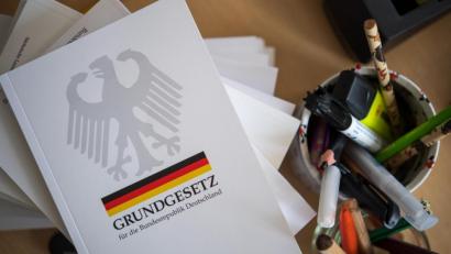 Symbolbild: Monika Skolimowska/dpa
Eine Ausgabe des Grundgesetzes der Bundesrepublik Deutschland liegt während des Unterrichts auf einem Tisch neben Schreibutensilien.