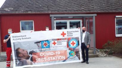 Bild: e
Vor dem Kümmersbrucker Testzentrum, dem Martin-Schalling-Haus in der Schillerstraße 3, rollen die Vertreter von BRK und Wasserwacht das Hinweisbanner schon mal probeweise auf.