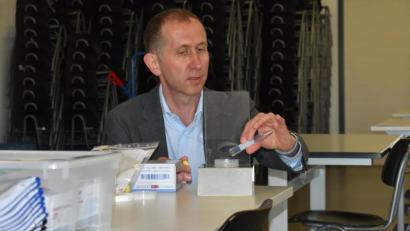 Bild: lue
Facharzt Dr. Michael Kabesch zeigt die Gurgel-Teststation an den Schulen. Ein Plastikbecher wird in ein Aluminumgestell mit Spritzschutz gestellt. Das Röhrchen mit der Flüssigkeit kann einfach darüber abgegossen werden.