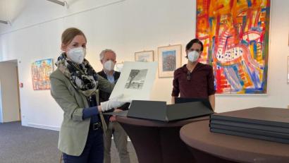 Bild: ass
Die erste offizielle Amberger Kunstmappe ist fertig. Ganz vorsichtig nimmt Julia Riß, die Leiterin des Stadtmuseums, Joe Ferstls "Unter schwerem Himmel" heraus. Kulturreferent Fabian Kern (Mitte) und A.K.T.-Vorsitzender Marcus Trepesch freuen sich auf mögliche Käufer.