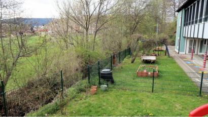 Bild: bsc
Ein Teil des Grundstücks links vom Zaun gehört der Gemeinde Friedenfels. Diese Fläche könnte während der Umbauarbeiten am Kinderhaus (rechts) als Ersatzspielgarten dienen. Das Erreichen wäre mit dem Bau einer kleinen Brücke über den Bach kein Problem, meint Bürgermeister Oskar Schuster.