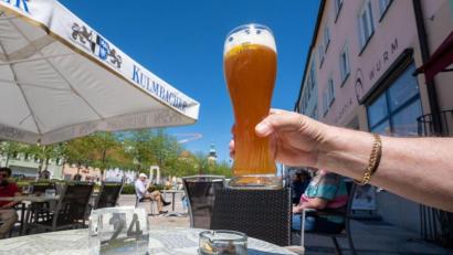 Bild: Armin Weigel/dpa
Ein Mann hält ein Glas mit Weißbier im Außenbereich von einer Eisdiele in Tirschenreuth hoch.