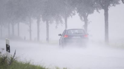 Symbolbild: Julian Stratenschulte/dpa
Ein Auto fährt bei Starkregen über eine Landstraße.