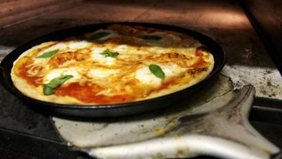 Symbolbild: Arno Burgi/dpa
Ein Pizzabäcker holt eine Pizza aus dem Ofen.