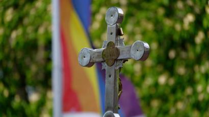 Bild: Henning Kaiser/dpa
Ein Kreuz steht bei einem Open-Air-Segnungsgottesdienst für Liebende vor einer Kirche. Im Hintergrund ist eine Regenbogenfahne zu sehen.