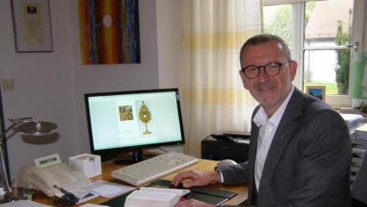 Bild: pz
Stadtpfarrer Thomas Vogl in seinem Arbeitszimmer im Pfarrbüro. Auf dem Bildschirm ist die Ansicht der Grußkarte mit der Monstranz als Motiv auf dem Titel zu sehen.