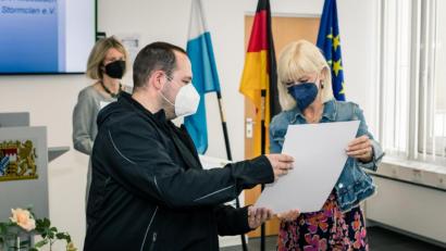 Bild: StMAS-Göttert
Manuel Balk, Vorsitzender des Vereins Mühlschleifhaisl, nimmt von Sozialministerin Carolina Trautner die Urkunde entgegen.