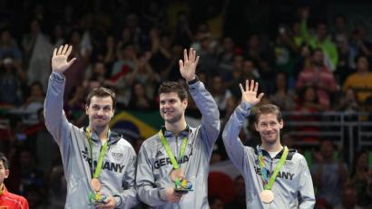 Bild: How Hwee Young/dpa
Timo Boll, Dimitrij Ovtcharov und Bastian Steger (von links), die Bronzemedaillengewinner im Tischtennis, winken 2016 ins Publikum. Die diesjährigen Medaillengewinner können sich das sparen. Es ist kein Publikum da.