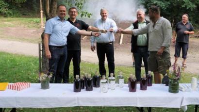 Bei der Verkostung am Meilerplatz: Mit „Gut Brand!“ stoßen Bürgermeister Erich Meidinger, Vorsitzender Josef Gilch, Landrat Richard Reisinger und Markus Dollacker als Vertreter des Naturparks Hirschwald mit einigen Vereinsmitglieder an.