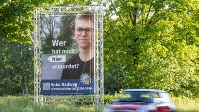 Archivbild: Daniel Karmann/dpa
"Wer hat mich hier ermordet?" steht auf einem großen Plakat mit Foto des Opfers neben dem Tatort.