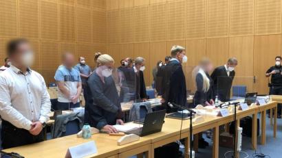 Archivbild: Ute Wessels/dpa
Die Angeklagten (1. Reihe 1.v.l., 2. Reihe 2.v.l. sowie 1. Reihe 4.v.l.) stehen im Gerichtssaal.