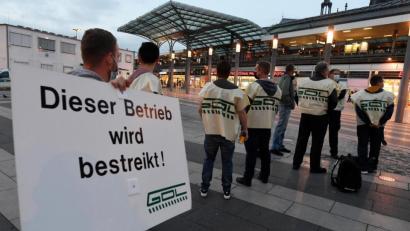 Bild: Roberto Pfeil/dpa
Mitglieder der Gewerkschaft der Lokführer (GDL) stehen mit einem Schild mit der Aufschrift «Dieser Betrieb wird bestreikt!» auf einem Bahnhofsvorplatz.