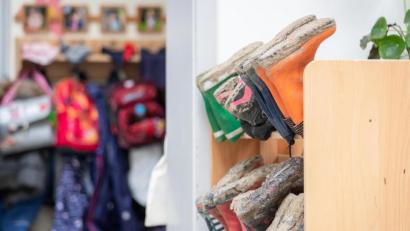 Symbolbild: Friso Gentsch/dpa
Kleidung und Taschen hängen an der Garderobe eines Kindergartens.