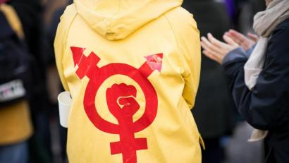 Symbolbild: Christian Charisius/dpa
Eine Frau trägt einen gelben Regenmantel mit einem Gender- und Protestsymbol bei einer Kundgebung zum Internationalen Frauentag.