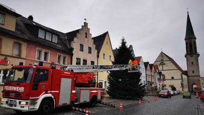 Bild: mde
Eine stattliche Nordmanntanne ziert den Kemnather Stadtplatz in dieser Weihnachtszeit. Ein Trupp der Feuerwehr Kemnath mit der Drehleiter und Mitarbeiter des städtischen Bauhofs sorgten am Donnerstagvormittag dafür, dass die Lichter am Weihnachtsbaum erstrahlen können.