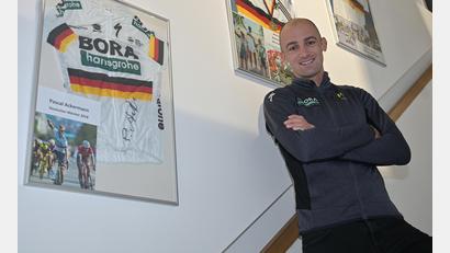 Bild: ref
An einer Wand im Fahrradgeschäft seiner Familie hat Andreas Schillinger einige besondere Andenken an seine Radsport-Karriere aufgehängt. Unter anderem seine beiden Goldmedaillen und Meistertrikots der deutschen Bergmeisterschaften 2017 und 2019 sowie ein unterschriebenes Trikot von Pascal Ackermann (links).