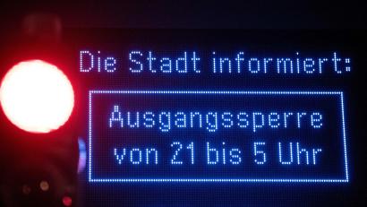 Archivbild: Fabian Strauch/dpa
Auf einem Display wird auf die „Ausgangssperre“ hingewiesen.