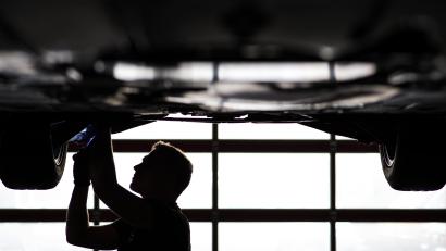 Symbolbild: David-Wolfgang Ebener
Ein Mechaniker arbeitet in einer Kfz-Werkstatt an der Unterseite eines Autos, das auf der Hebebühne steht.