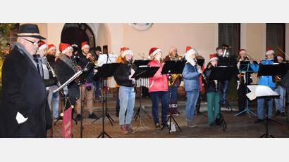 Bild: oe
Die Blaskapelle verbreitet musikalisch vorweihnachtliche Stimmung auf dem Ammerthaler Dorfplatz. Bürgermeister Anton Peter (links) trägt besinnliche Texte vor.