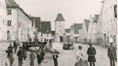 Bild: Stadtarchiv Sulzbach-Rosenberg
Das Rosenberger Tor war bis zu seinem Abbruch 1871 der östliche Zugang zur Sulzbacher Innenstadt. Unsere historische Aufnahme stammt vermutlich aus der Mitte des 19. Jahrhunderts und zeigt spielende Kinder und erwachsene Bürger auf der mit Kopfstein gepflasterten Rosenberger Straße. Im Hintergrund das mit Strebepfeilern aus Bruchstein verstärkte Tor.