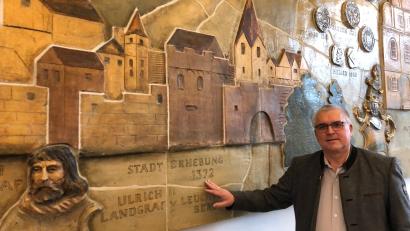 Bild: mis
Pfreimds Erster Bürgermeister Richard Tischler vor dem Wandkunstwerk im Pfreimder Stadtratssaal. Das Werk zeigt die bedeutendsten geschichtlichen Etappen Pfreimds. Dabei darf natürlich die Stadterhebung im Jahre 1372 nicht fehlen.