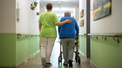 Symbolbild: Sina Schuldt/dpa
Eine Pflegefachkraft mit einer Seniorenheim-Bewohnerin bei einem Spaziergang auf dem Flur.