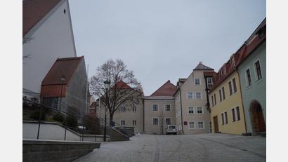 Bild: wel
Umgestaltungsmaßnahmen zur Kirche St. Josef (links) wie begrünte Spaliere an Turm sowie der Sakristei und ein aktiver Brunnen vor dem Pfarrhof sollen den Platz aufwerten. Auf der Rückseite des gelben Erweiterungsbaus des Rathauses "Im Berg 7" wird ein Innenhof gestaltet, der mit Grünflächen, Sitzbänken und einem Schatten spendenden Baum in der Mitte zum Verweilen einlädt.