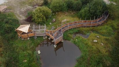 Bild: Stefan Hilgenfeld/exb
Ein Blick auf das Umweltareal: Entstanden ist ein Teich, ein Damm aufgeschichtet, eine künstliche Industriebrache sowie ein Erlebnissteg mit Hängebrücke und Sitzbereich. Infotafeln klären über das Grüne Band auf.