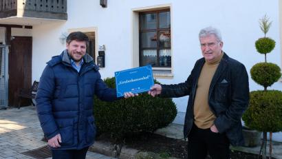 Bild: mab
Bürgermeister Peter Neumeier (links) übergibt das Hausnamenschild (Gruberhansenhof) an Eigentümer Manfred Röhl.