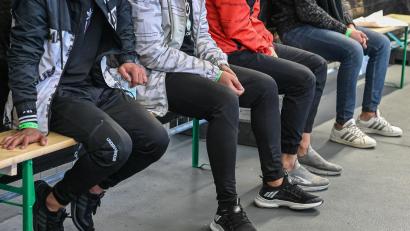 Symbolbild: Patrick Pleul
Migranten sitzen bei der Bundespolizei auf Bierbänken und warten.