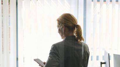 Bild: Annette Riedl/dpa
Eine Frau steht in einem Bürozimmer und hält ein Smartphone in der Hand (gestellte Szene).