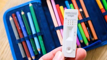 Bild: Julian Stratenschulte/dpa/Illustration
Ein Corona-Selbsttest wird über dem Federmäppchen eines Schülers gehalten.