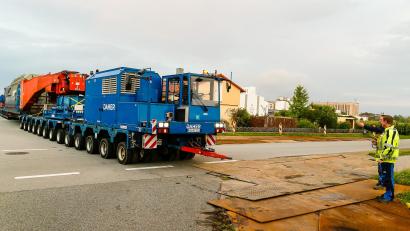Bild: Hösamer
Gut 55 Meter und rund 546 Tonnen schwer lang ist der Schwerlastzug, der am Montagabend vom Müllkraftwerk durch die Alustraße (Bild) Richtung Umspannwerk Büchelkühn rollt. Transportiert wird ein 273 Tonnen schwerer Trafo, der in einem Tieflader mit Tragschnäbeln (rot) auf zwei jeweils 13-achsigen, je 700 PS starken Zugmaschinen ruht.