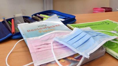 Bild: Patrick Pleul/dpa-Zentralbild/dpa/Symbolbild
Masken liegen in einem Klassenzimmer auf einem Schulbuch.
