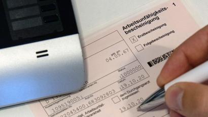 Symbolbild: Paul Zinken/dpa-Zentralbild/dpa
Ein Mitarbeiter einer Arztpraxis füllt eine Arbeitsunfähigkeitsbescheinigung aus.