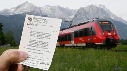 Symbolbild: Angelika Warmuth
Ein Mann hält ein 9-Euro-Ticket in der Hand, im Hintergrund fährt ein Zug der Deutschen Bahn vor der Bergkulisse des Wettersteingebirges vorbei.