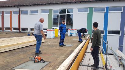 Bild: gi
Die Sanierung des Flachdaches des Aula-Gebäudes der Grundschule Moosbach ist voll im Gange; hier die Zimmerei-Firma im Gespräch mit Hausmeister Wolfgang Piehler (links).