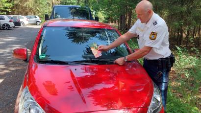 Bild: Polizeiinspektion Tirschenreuth/exb
Erster Polizeihauptkommissar Günther Burkhard klemmt ein Flugblatt an die Windschutzscheibe eines parkenden Autos beim Rothenbürger Weiher.