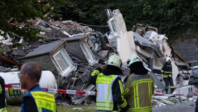 Bild: Bjoern Braun/dpa
Feuerwehrleute stehen vor dem eingestürzten Haus.