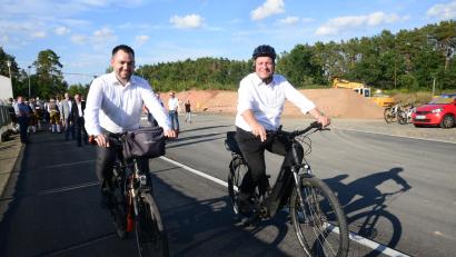 Bild: bey
Bürgermeister Sebastian Hartl (links) und Staatsminister Christian Bernreiter schauen sich per Praxix den neuen Radweg bis zur BAB A 93 an. Im Hintergrund sind die Ehrengäste, die ohne Fahrrad gekommen sind.