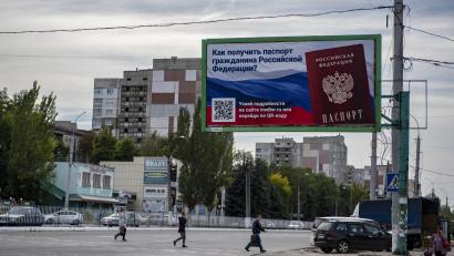 Bild: dpa/AP
Menschen überqueren in der Region Luhansk eine Straße mit einem Plakat mit der Aufschrift "Wie man den Pass eines russischen Bürgers bekommt".