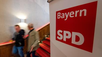 Symbolbild: Lino Mirgeler/dpa
Zwei Männer gehen am Logo der SPD Bayern vorbei. Der Umgang der Landeschefs mit dem Abgang von Taşdelen wirft kein gutes Licht auf die Partei, meint Jürgen Umlauft.