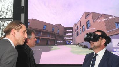 Bild: phs
Mit einer Virtual-Reality-Brille geht Gesundheitsminister Klaus Holetschek (rechts) durch das zentrale Gebäude des Alia-Areals. Was er dabei sieht, erläutern ihm Projektleiter David Rester und Architekt Christian Schönberger (von links) näher.