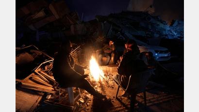 Bild: Khalil Hamra/AP/dpa
Menschen wärmen sich an einem Feuer vor Gebäuden, die bei den Erdbeben in der Türkei zerstört wurden.