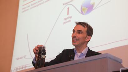 Bild: Wolfgang Steinbacher
Professor Markus Beckmann erklärt einen Kipppunkt: Irgendwann fällt die Flasche in seiner Hand um. Dann schafft sie es nicht mehr, aus eigener Kraft in ihre Ausgangsposition zurückzukehren.