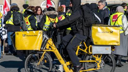 Bild: David Inderlied/dpa
Ein Postbote radelt in Bielefeld an Streikenden einer Verdi-Aktion vorbei.