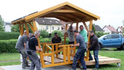 Bild: lst/exb
Kräftige Jungs der Flosser Siedlergemeinschaft legten am Dienstagabend mächtig Hand an und platzierten das neue schattenspendende Holzhaus für Familien und Kinder auf dem Spielplatz im Ortsteil Ziegelhütte.