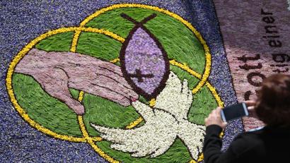 Bild: Patrick Seeger/dpa
Eine Frau fotografiert an Fronleichnam während der Prozession Kirchenmotive in einem Blumenteppich.